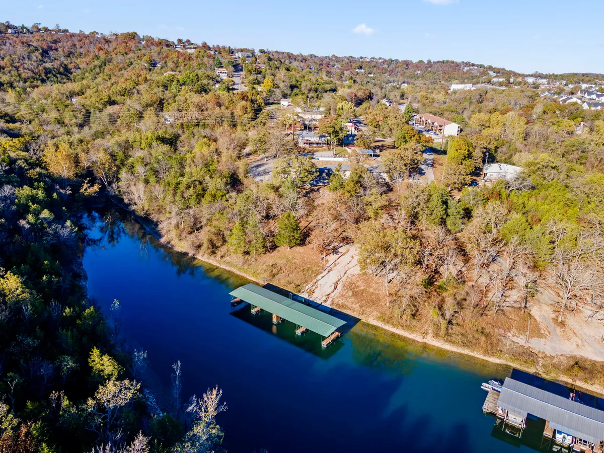 A serene lakeside dock stretches over the water, surrounded by trees and rolling hills. The dock is a clear focal point for fishing and launching boats, with the peaceful water reflecting the natural beauty of the area.