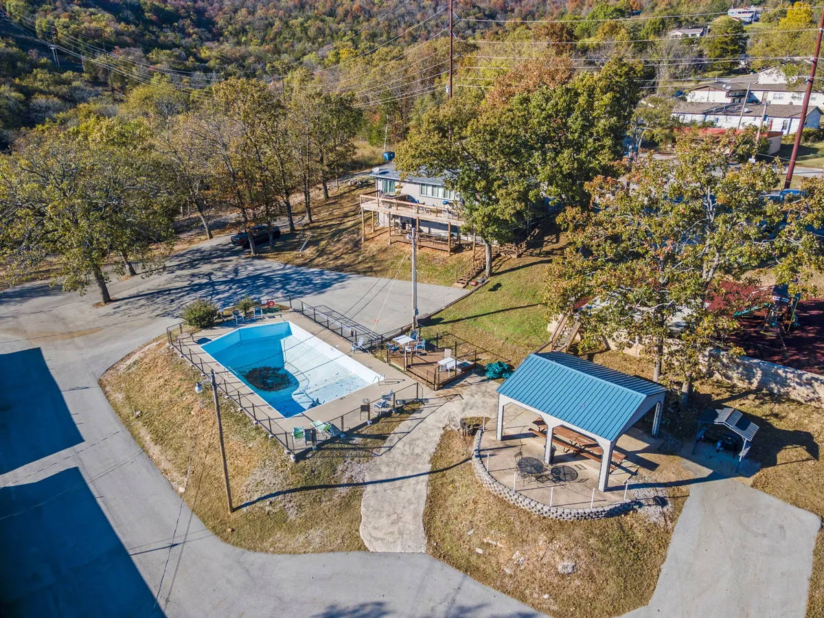 A sparkling outdoor swimming pool is the centerpiece of this image, framed by surrounding trees and an inviting outdoor gazebo. The space is designed for sunbathing, swimming, and relaxed social gatherings, suggesting a summer paradise ideal for both families and couples.