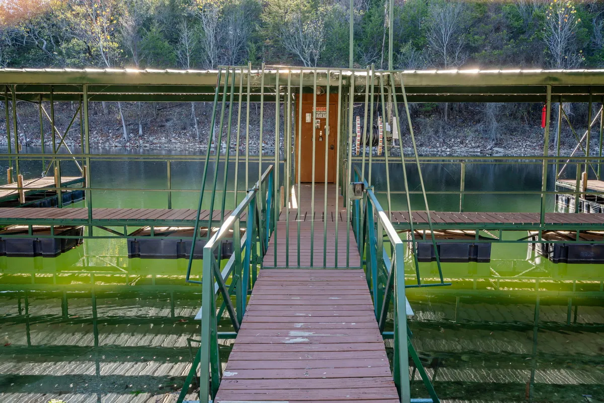 A peaceful view of a wooden walkway leading out to a boathouse, with gentle water all around and golden reflections from the setting sun. The dock area is inviting for both fishing and relaxing near the water’s edge, in a setting where pets could easily be included in the fun.