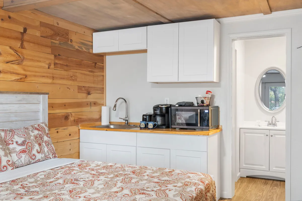 The photo spotlights a kitchenette with wooden wall paneling, a patterned bed nearby, and essential appliances (including a microwave, mini-fridge, and coffee maker). The scene radiates a comfortable, homey vibe, highlighting how cooking, relaxing, and entertaining seamlessly blend in this space.