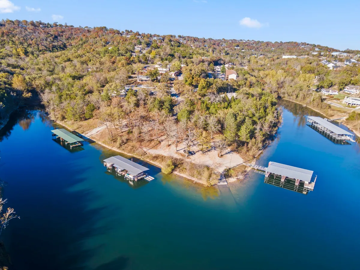 A wide, serene scene of the lake with docks extending into the water, surrounded by leafy trees and a handful of houses dotting the hillside. The early morning mist and abundant shoreline provide ample space for dogs to roam and play fetch in the open.