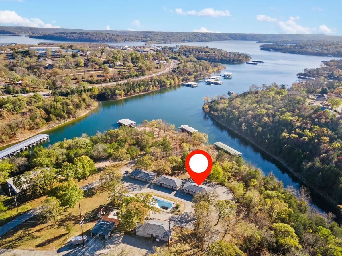 An expansive view of the sparkling lake bordered by trees, with a swimming pool and houses visible in the background. The image evokes relaxation and recreation, with the pool as a centerpiece and the lake promising water activities just beyond.