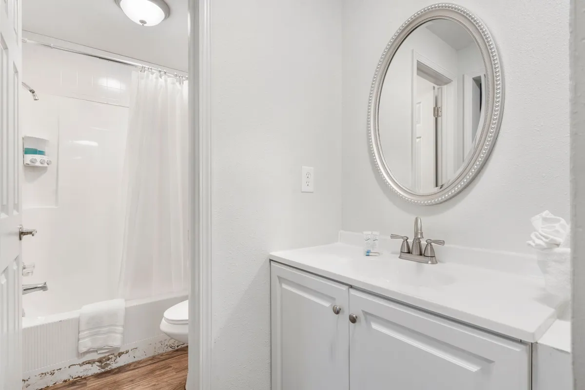 A clean and serene bathroom interior showcasing a circular mirror, white vanity, and a bathtub with a shower. The design is simple, fresh, and practical, providing an inviting space for daily routines and relaxation.
