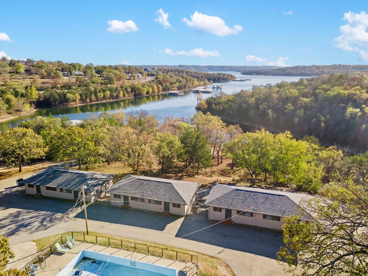 A relaxed resort setting with a swimming pool overlooking a riverside view, framed by tall trees and rustic cabins. The pool area offers a place for couples to lounge together and enjoy nature’s beauty.