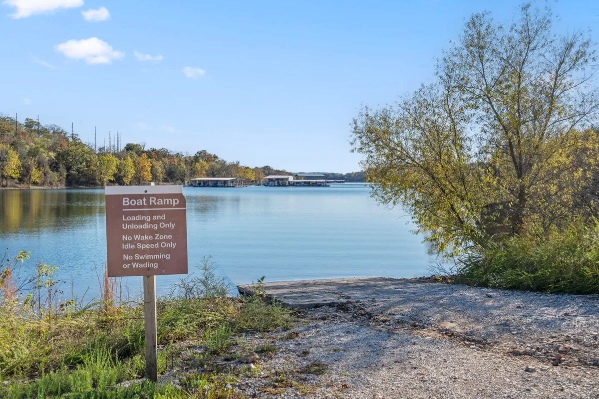 The exterior scene features a boat ramp leading to calm water, bordered by trees, plus clear signage indicating boat launching. The area is peaceful and welcoming, making it an ideal spot for both fishing and setting out on a boating adventure.